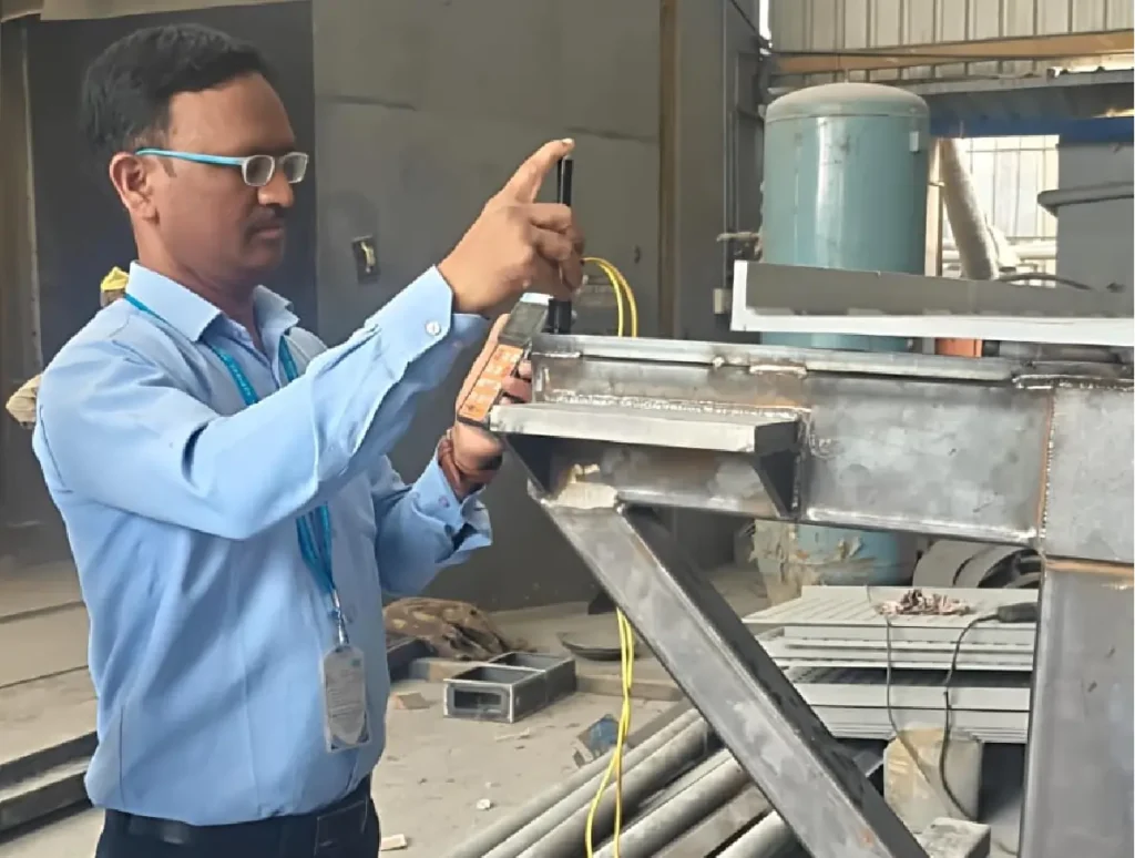 Trinity NDT engineer performing on-site Leeb portable hardness testing on a structural steel weld joint at a fabrication facility in India